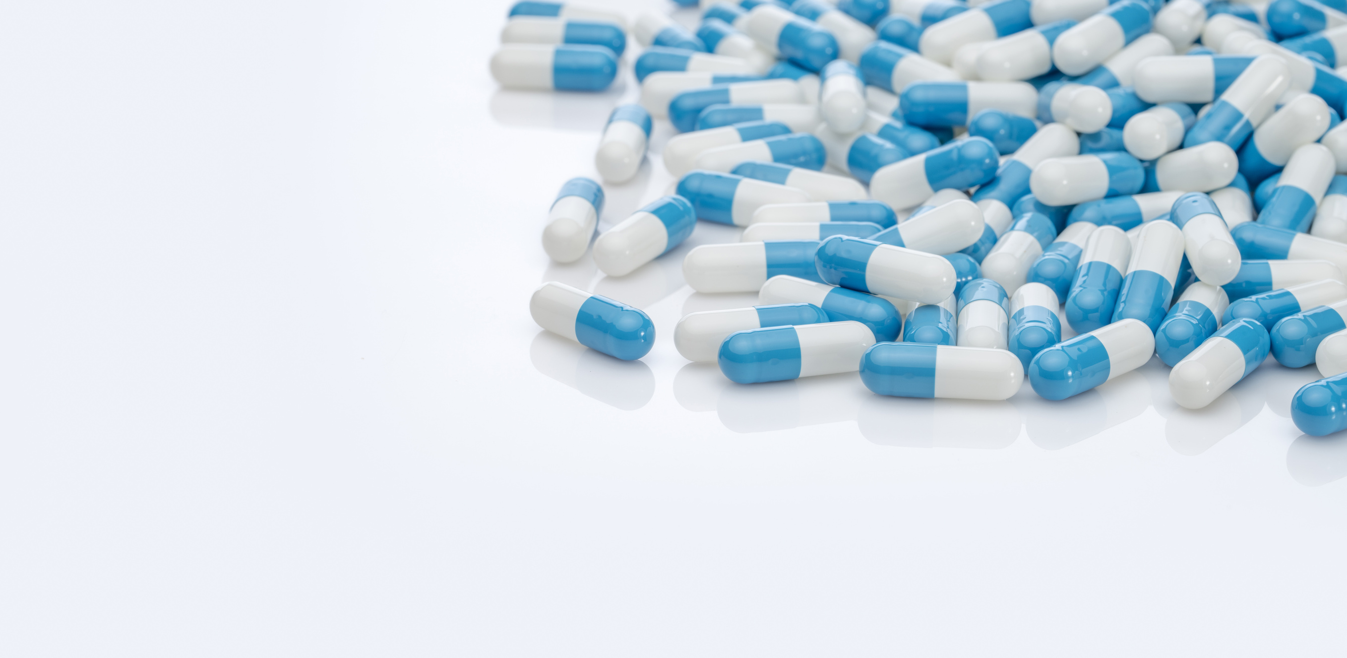 Blue-white antibiotic capsule pills on white background. Pile of antibiotic drug. Antibiotic drug resistance. Prescription drugs. Healthcare and medicine. Pharmaceutical industry. Pharmacy product.